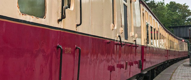 side view of a long train with a beige coloured top half and red lower half