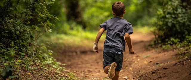 Boy running along a path in the woods on a sunny day