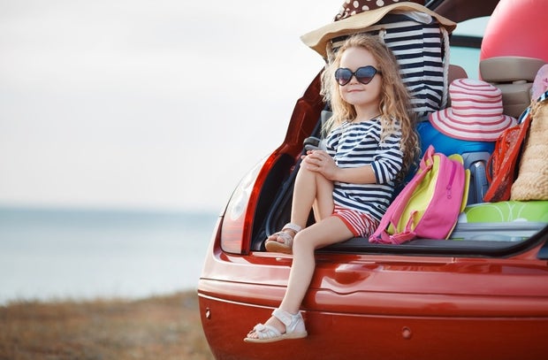 Child sitting on the edge of the packed boot of the car 