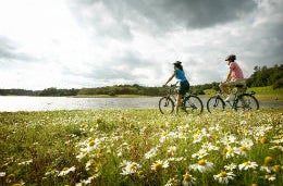 Five Unforgettable UK Cycling Holidays Couple cycling through green fields in the sun.